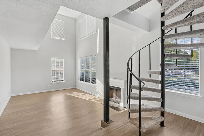 Bright and airy living space with elegant spiral staircase and large windows, offering abundant natural light and an open, modern feel.