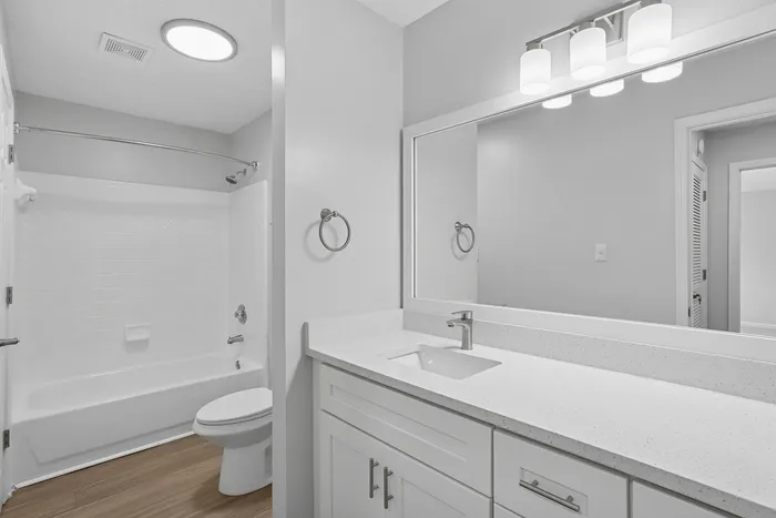 Sleek modern bathroom featuring elegant fixtures, pristine white countertops, large vanity mirror, and a stylish combination of ceramic and wood-style flooring.