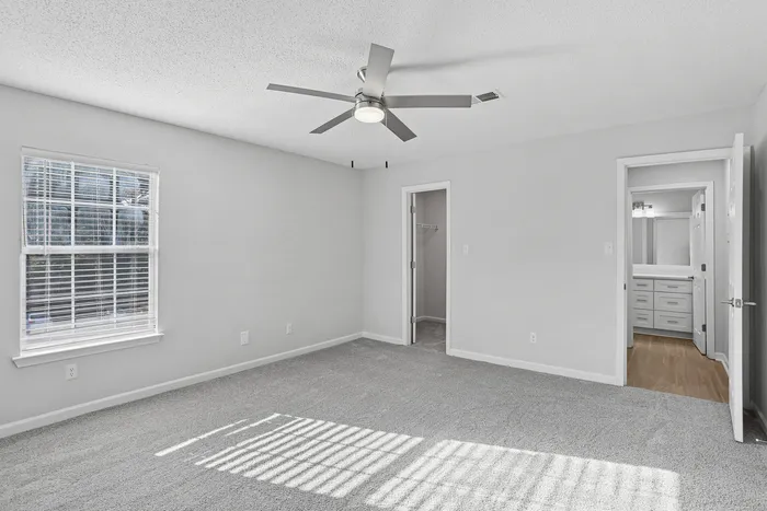 Bright and spacious bedroom with plush carpeting, modern ceiling fan, and a walk-in closet, leading to a sleek bathroom.