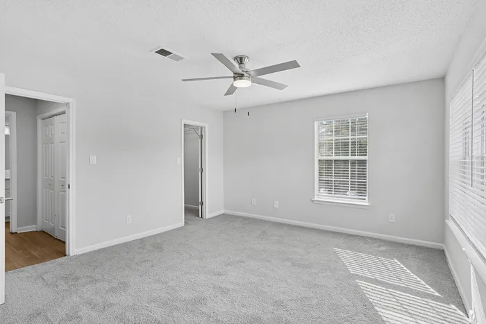 Bright and airy bedroom with soft carpeting, ceiling fan, and large windows offering plenty of natural light.