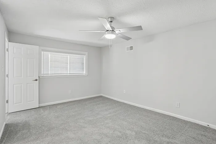 Bright, airy room featuring modern ceiling fan, plush carpet, and large window with blinds.