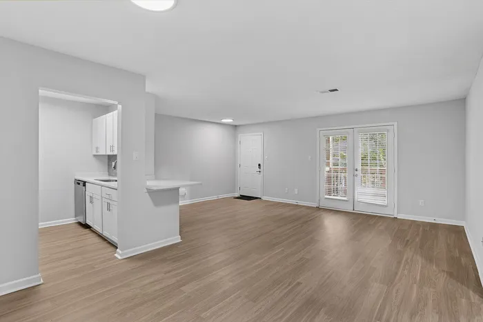 Bright open-concept living space with sleek modern kitchen, elegant light fixtures, and spacious hardwood flooring leading to inviting French doors.
