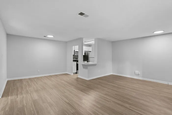 Spacious open living room with elegant wood flooring and a cozy adjoining kitchen featuring modern appliances.