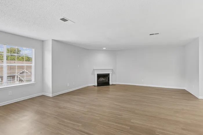 Spacious living room with elegant wooden flooring and a cozy fireplace, bathed in natural light from large windows.