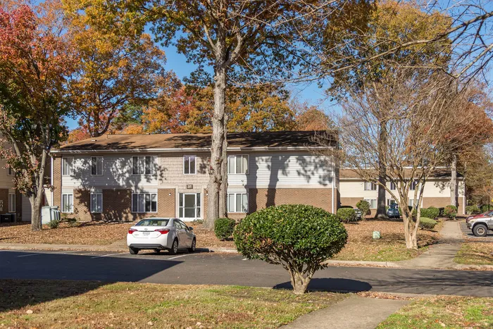 Charming two-story apartment complex surrounded by vibrant autumn trees, featuring a well-maintained front yard and ample parking.