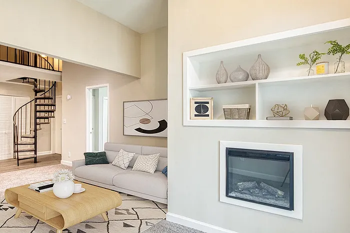 Chic living room with a modern spiral staircase, cozy fireplace, and elegant decor. Features a comfortable beige sofa and stylish shelving in a contemporary setting.