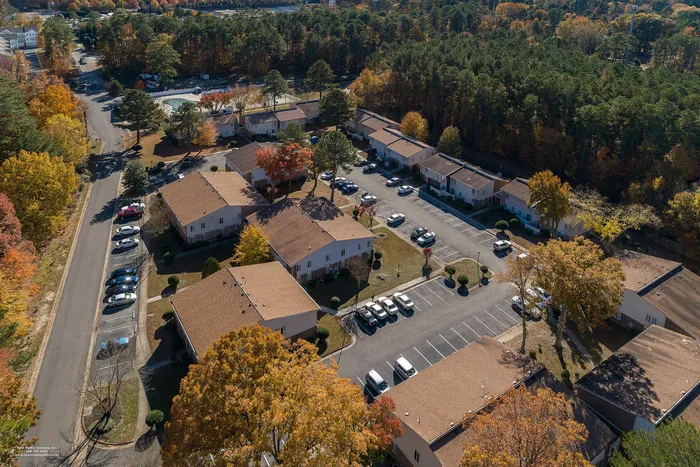 Charming aerial view of a serene apartment complex nestled among vibrant autumn foliage, showcasing ample parking and spacious buildings.
