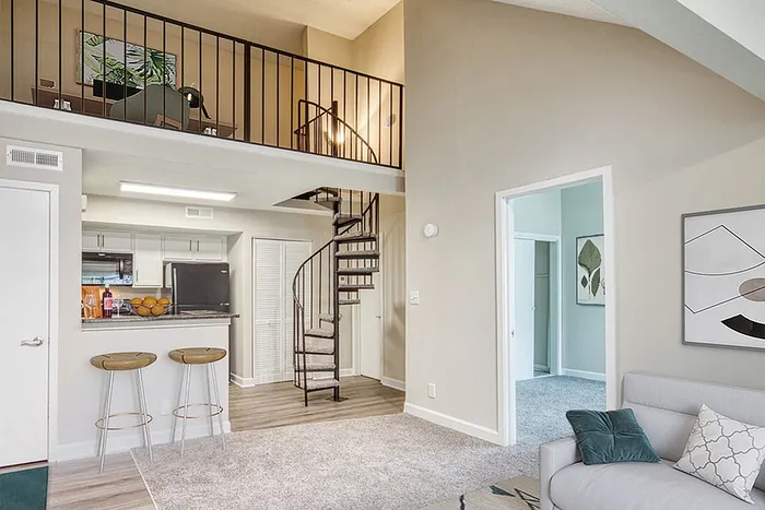 Modern apartment interior featuring a cozy living room, open kitchen with bar seating, and a stylish spiral staircase leading to an upper loft.