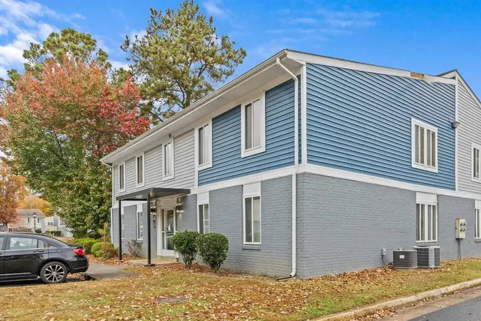 Charming blue and gray townhouse with lush trees and a welcoming entrance, ideal for cozy living.