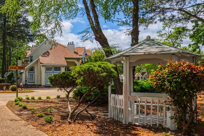 Charming residential scene featuring a cozy gazebo amidst lush greenery and a picturesque house with a gabled roof, offering serene and inviting surroundings.