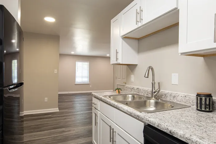 Modern kitchen with sleek granite countertops, white cabinetry, and open layout flowing into a bright living area.