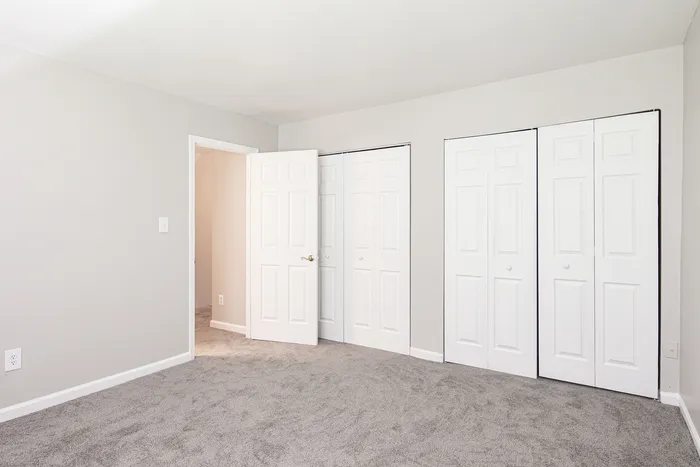 Bright and spacious bedroom with plush grey carpeting and generous closet space, perfect for stylish living.