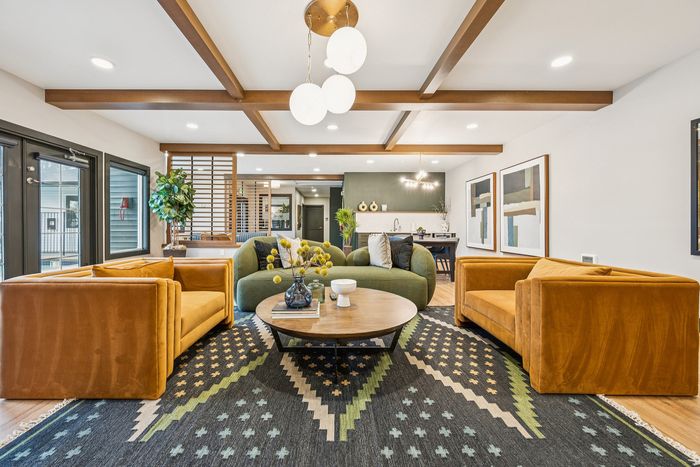 Chic living area with modern decor, featuring mustard velvet sofas, a round wooden coffee table, and geometric-patterned rug under exposed ceiling beams.