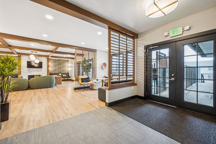 Modern apartment lounge with stylish decor, wooden floors, cozy seating, and natural light from large windows.