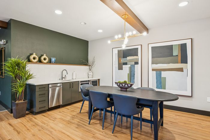 Contemporary dining area with elegant wooden flooring, modern art pieces, and a stylish kitchen setup with stainless steel fixtures.