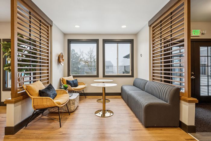 Chic modern seating area with stylish chairs, sleek gray sofa, and contemporary wooden accents, flooded with natural light from big windows.