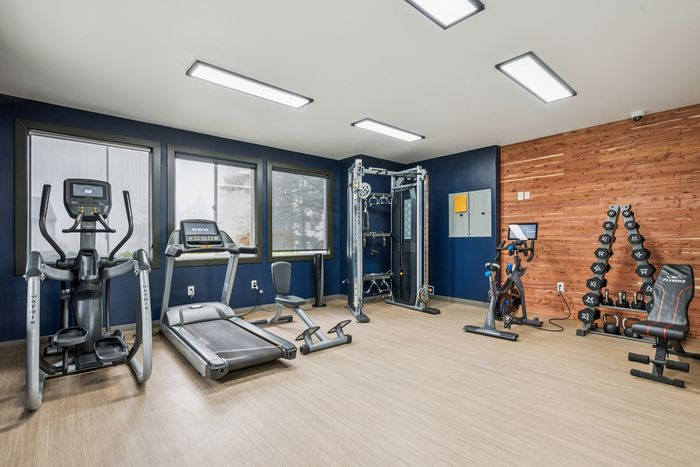 Modern fitness room with state-of-the-art gym equipment, including a treadmill, elliptical, and weight station in a stylish wooden-accented room.