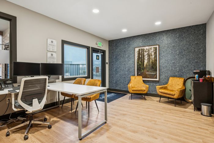 Contemporary office space featuring dual computer monitors, sleek white desk, plush mustard armchairs, and elegant wood flooring, perfect for a modern work environment.