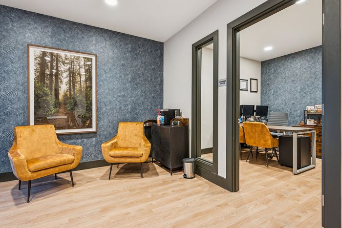 Chic office interior showcasing two stylish mustard chairs against a textured blue wall with serene forest artwork, highlighting a welcoming and professional atmosphere.
