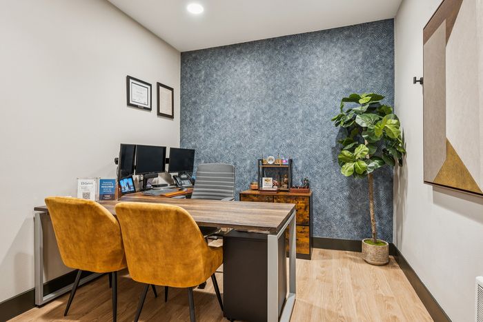 Sophisticated home office with modern desk, dual monitors, plush mustard chairs, and chic botanical decor.