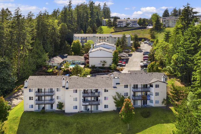 Charming apartment complex nestled in lush woodland with modern buildings and scenic surroundings.