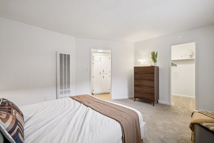 Elegant bedroom featuring a plush bed with stylish linens, a sleek wooden dresser, and a spacious walk-in closet, all in a serene ambiance.