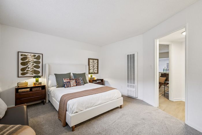 Elegant bedroom with plush carpet, featuring a cozy bed, stylish side tables, and modern wall art in a bright, inviting space.
