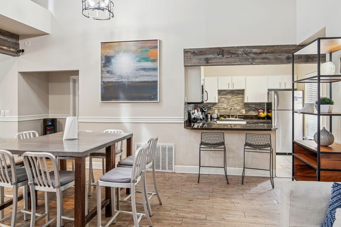 Modern open-plan dining and kitchen area with a high table, stylish bar stools, and contemporary art, featuring sleek wooden floors and ample natural light.