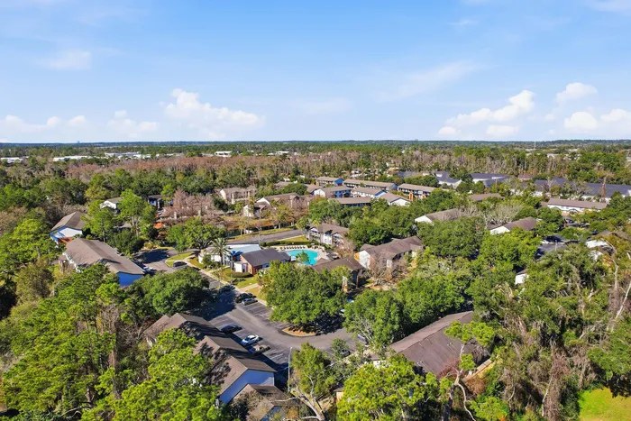 Townhomes at TSC Bird's-eye view of a lush, tranquil residential community with a sparkling central pool, surrounded by charming homes and verdant trees under a bright blue sky.