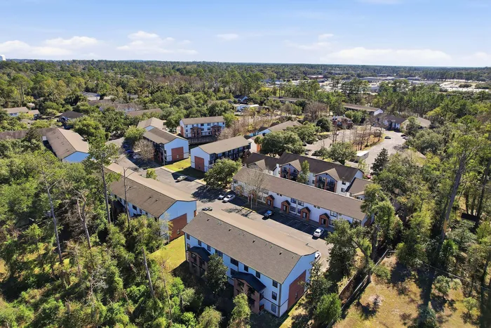 Townhomes at TSC Charming aerial view of a lush, green apartment community nestled in a tranquil, wooded area with modern buildings and ample parking.