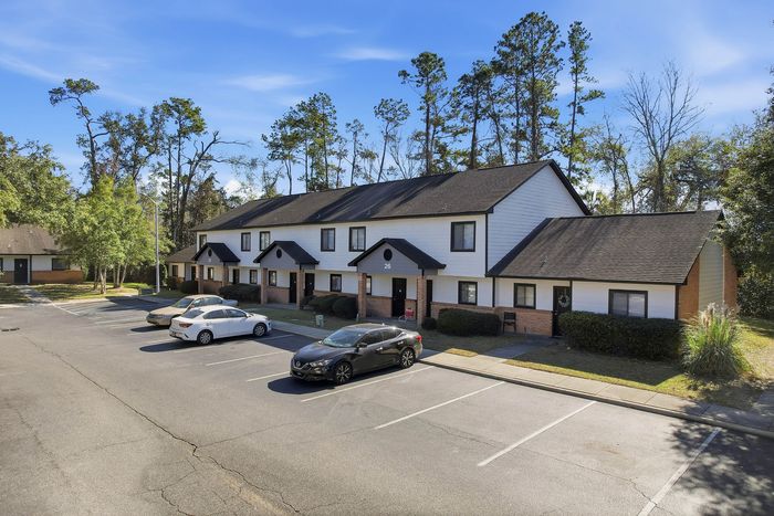 Townhomes at TSC Inviting townhouse complex with charming white facades, surrounded by lush greenery and ample parking space under a clear blue sky.