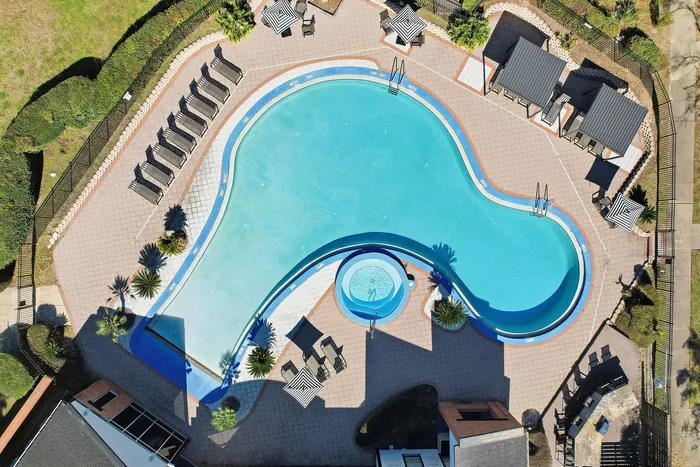 Townhomes at TSC Elegant aerial view of a luxurious outdoor swimming pool with cozy lounging areas, surrounded by lush greenery and stylish pavilions.