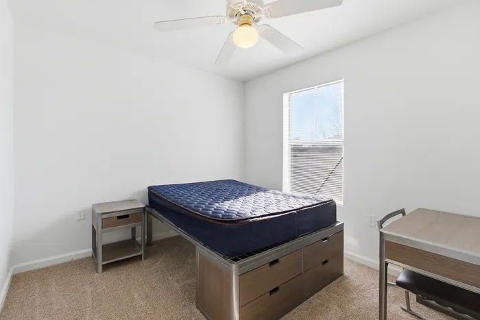 Townhomes at TSC Bright and airy bedroom with a cozy bed, desk, and ample natural light through large window, perfect for restful nights.