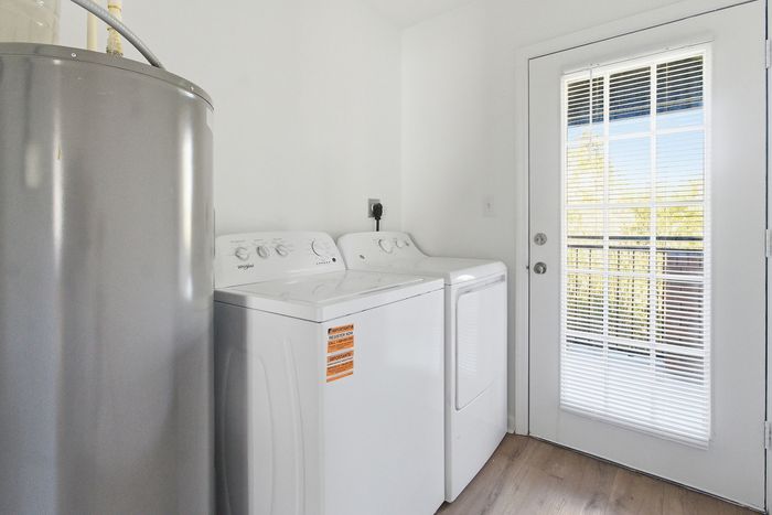 Townhomes at TSC Bright laundry room with modern washer and dryer, large water heater, and glass door leading to a sunny outdoor area.