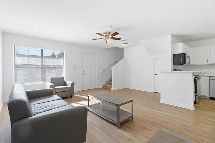 Townhomes at TSC Bright and airy living room with modern gray sofas, open kitchen concept, wood flooring, and elegant ceiling fan.