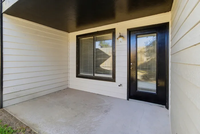 Townhomes at TSC Charming apartment exterior featuring a cozy covered patio with a sleek black-trimmed window and door, ideal for relaxation.