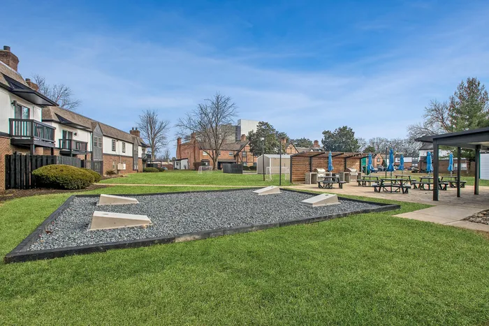 Charming outdoor communal area with lush green lawns, picnic tables under umbrellas, and unique architectural townhouses in the background.