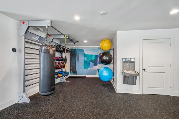 Modern apartment gym with sleek equipment and vibrant decor, featuring punching bags, exercise balls, and a water station.