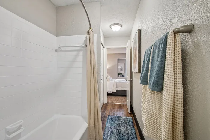 Inviting bathroom with elegant white tiles, a classic bathtub, and a cozy view into a warmly lit bedroom.
