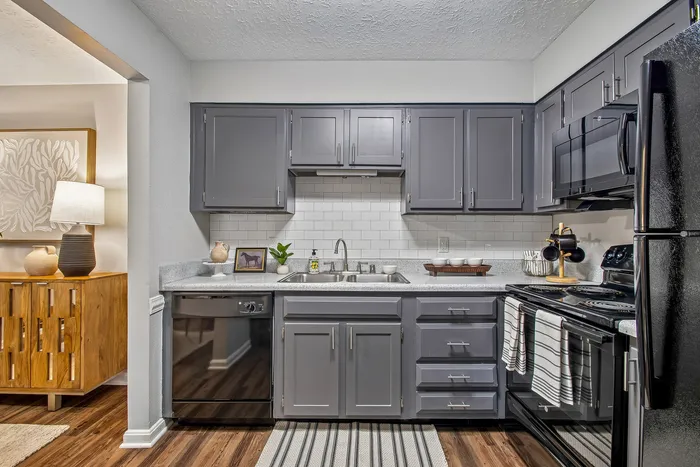 Modern kitchen with sleek gray cabinets, white subway tile backsplash, and gleaming countertops. Features stylish wooden flooring and contemporary decor.