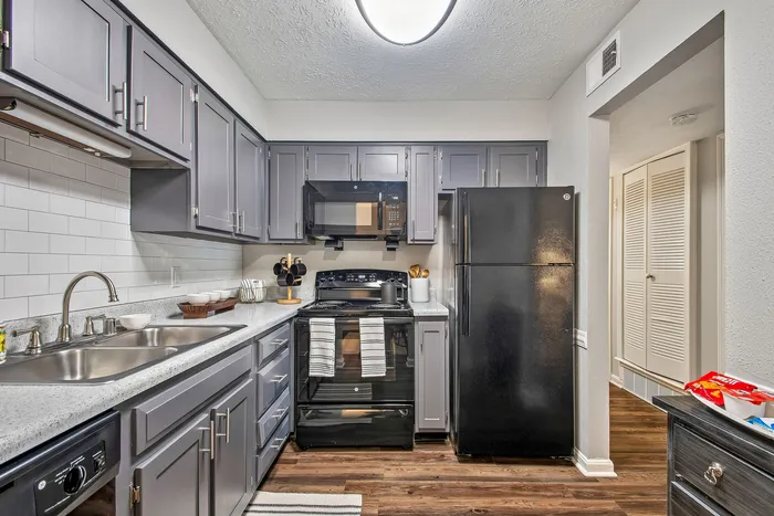 Modern kitchen design with sleek gray cabinets, stainless steel double sink, and black appliances on rich hardwood floors.