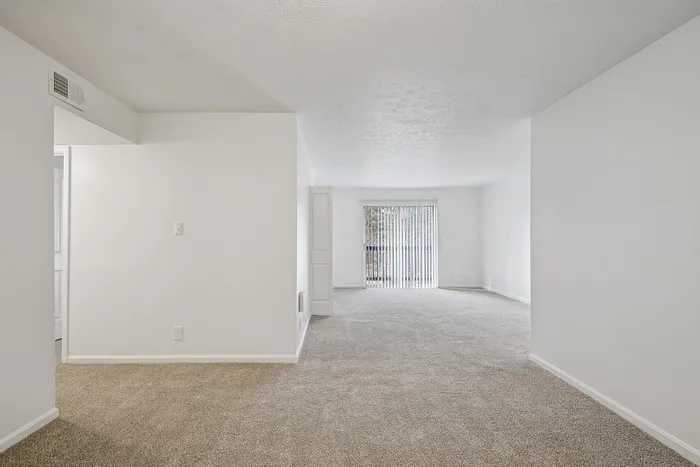 Bright, spacious living area with plush carpet and large sliding glass doors opening to a scenic view.