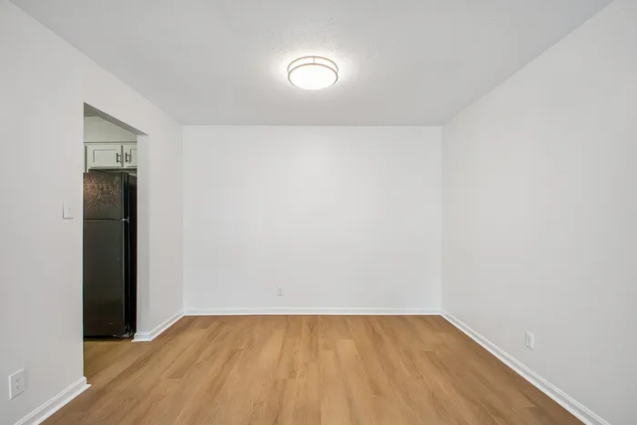 Bright and inviting room with elegant wooden flooring and crisp white walls, adjacent to a modern kitchen with sleek appliances.