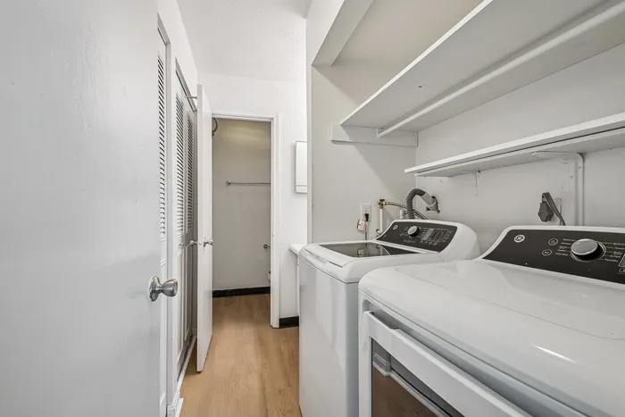 Sleek laundry room featuring modern appliances, ample shelving, and a stylish wood floor.