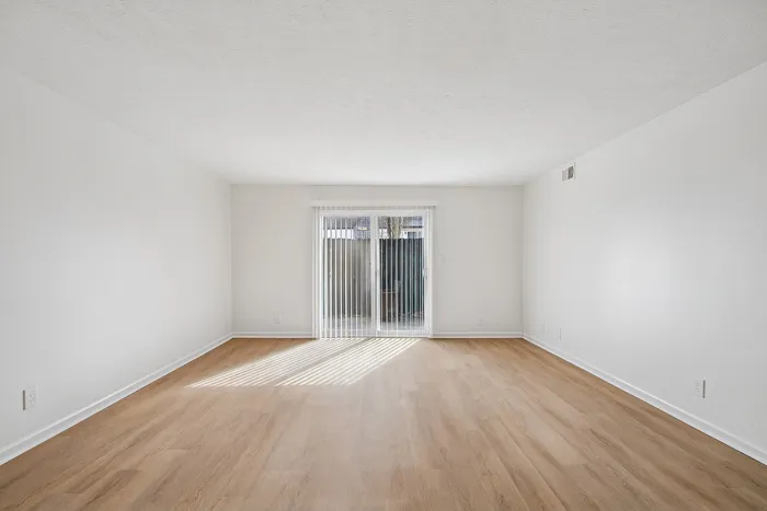 Bright and spacious living room with elegant hardwood floors, featuring large glass doors opening to a serene outdoor view.