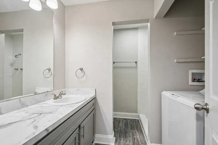 Modern bathroom with elegant marble countertop, sleek gray cabinetry, and an in-unit washer for convenience.