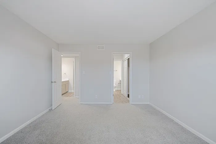 Bright, spacious bedroom with plush carpeting, featuring two doorways leading to a modern bathroom and a closet.