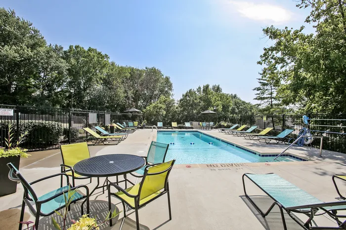 Inviting outdoor pool area surrounded by lush greenery with modern lounge chairs and seating, perfect for relaxation and social gatherings.