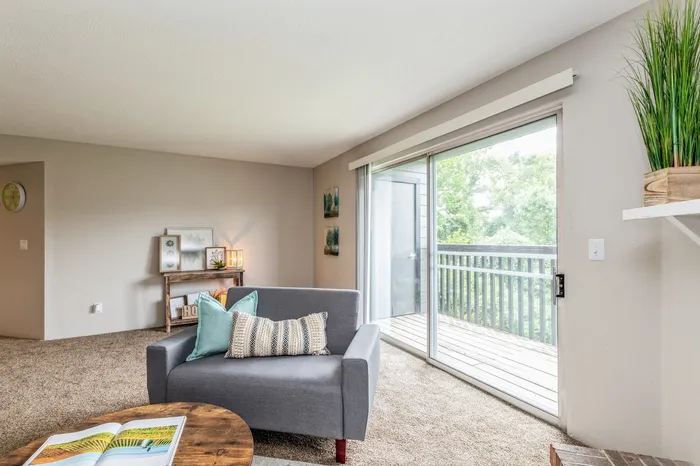 Bright and inviting living room with a stylish gray sofa, cozy pillows, and large sliding glass doors leading to a serene balcony with greenery views.