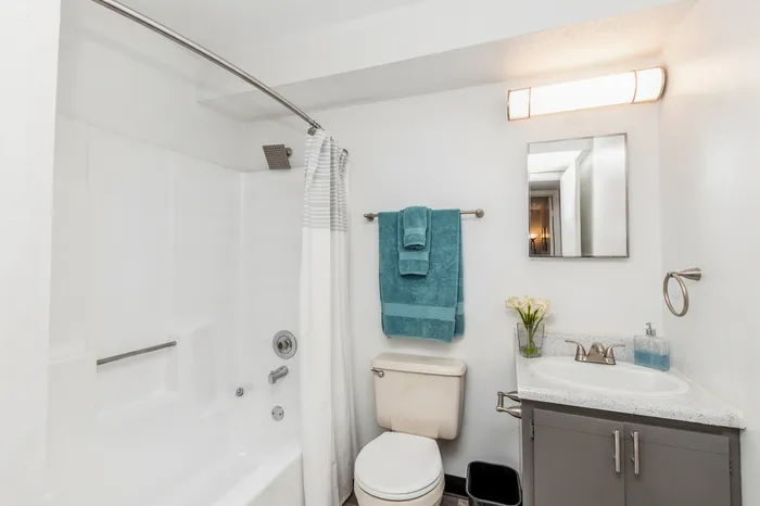 Bright, modern bathroom with sleek fittings, featuring a white bathtub and elegant vanity, accented by teal towels for a refreshing touch.